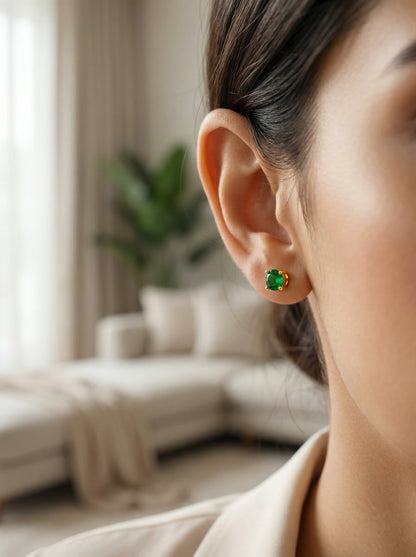 Close-up of a person wearing green 18k gold plated earrings with a blurred indoor background