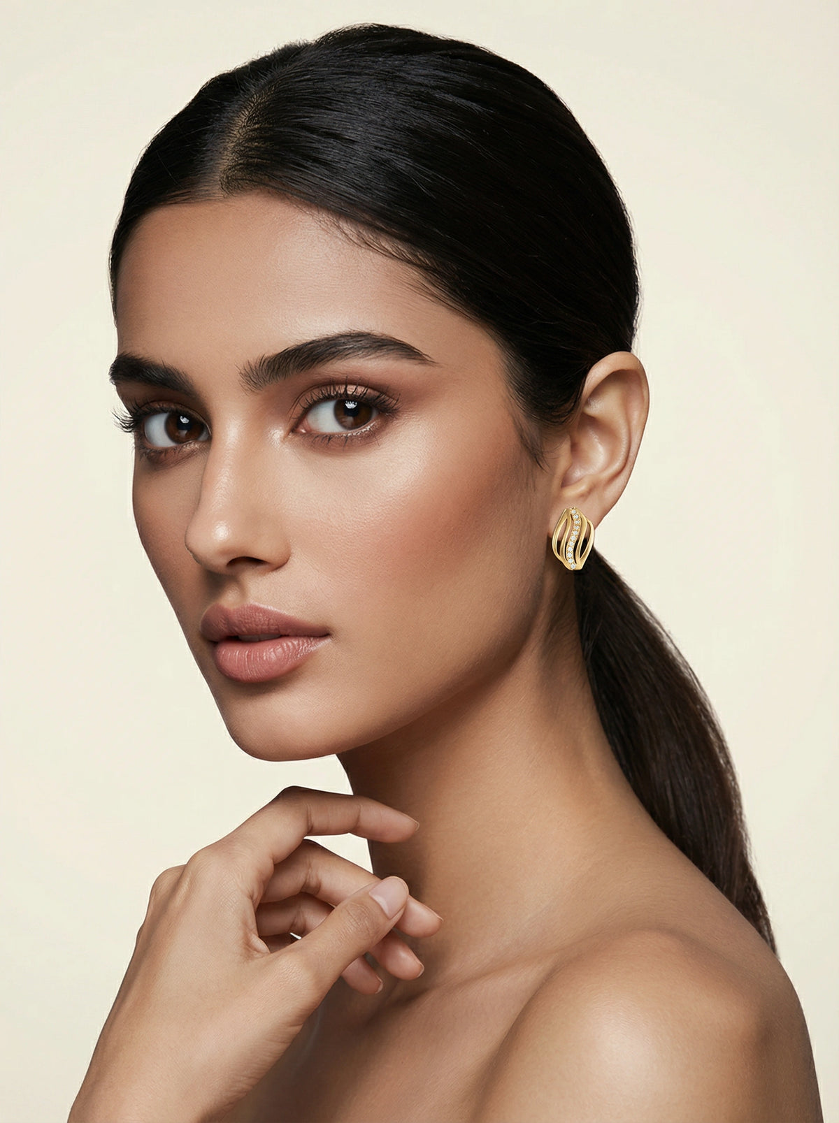 woman with a ponytail wearing 18k gold plated earrings against a beige background