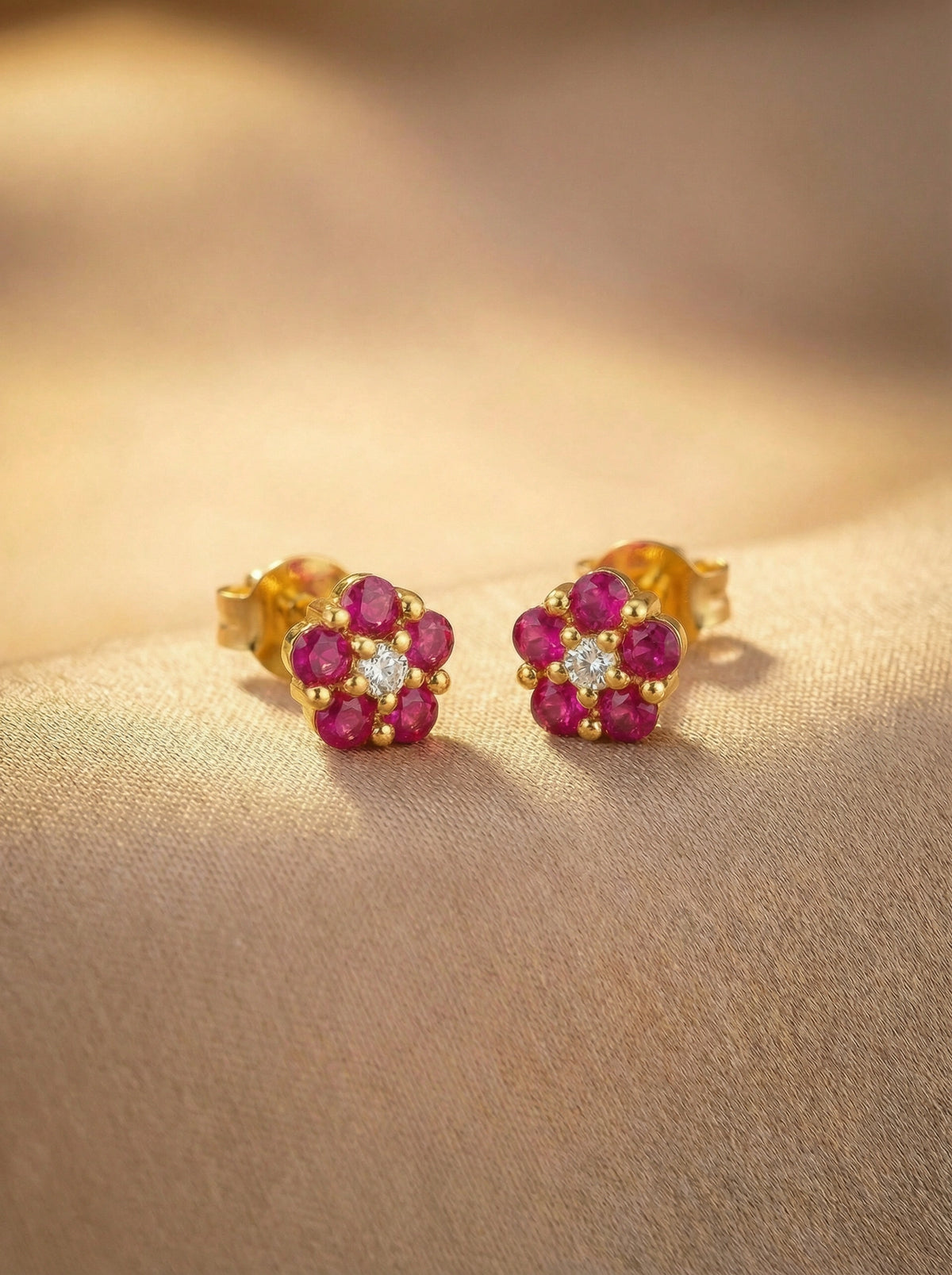 18k gold plated earrings with red gemstones on a beige surface