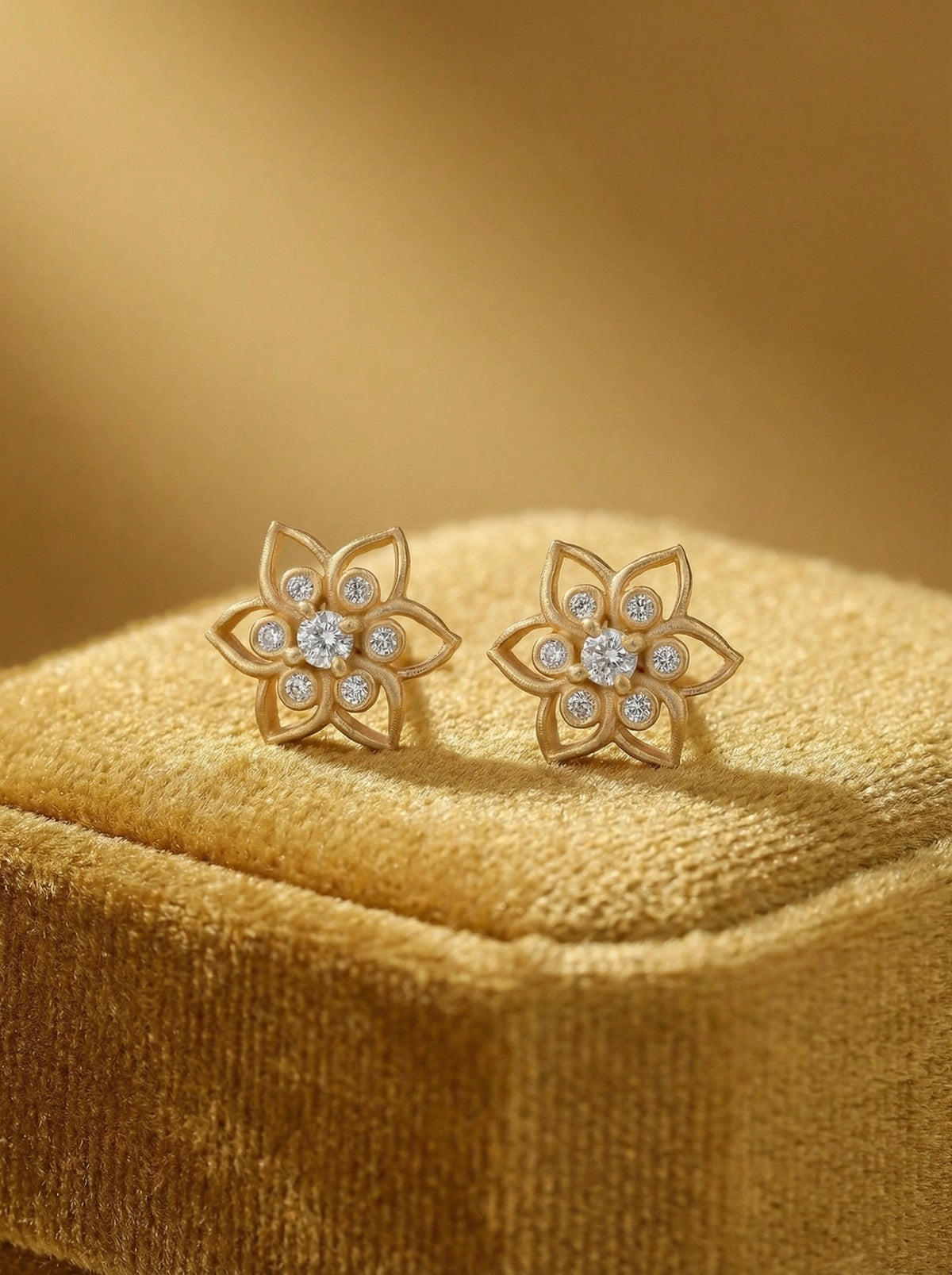 pair of  18k gold plated flower-shaped earrings with diamond-like stones on a matching yellow cushion.