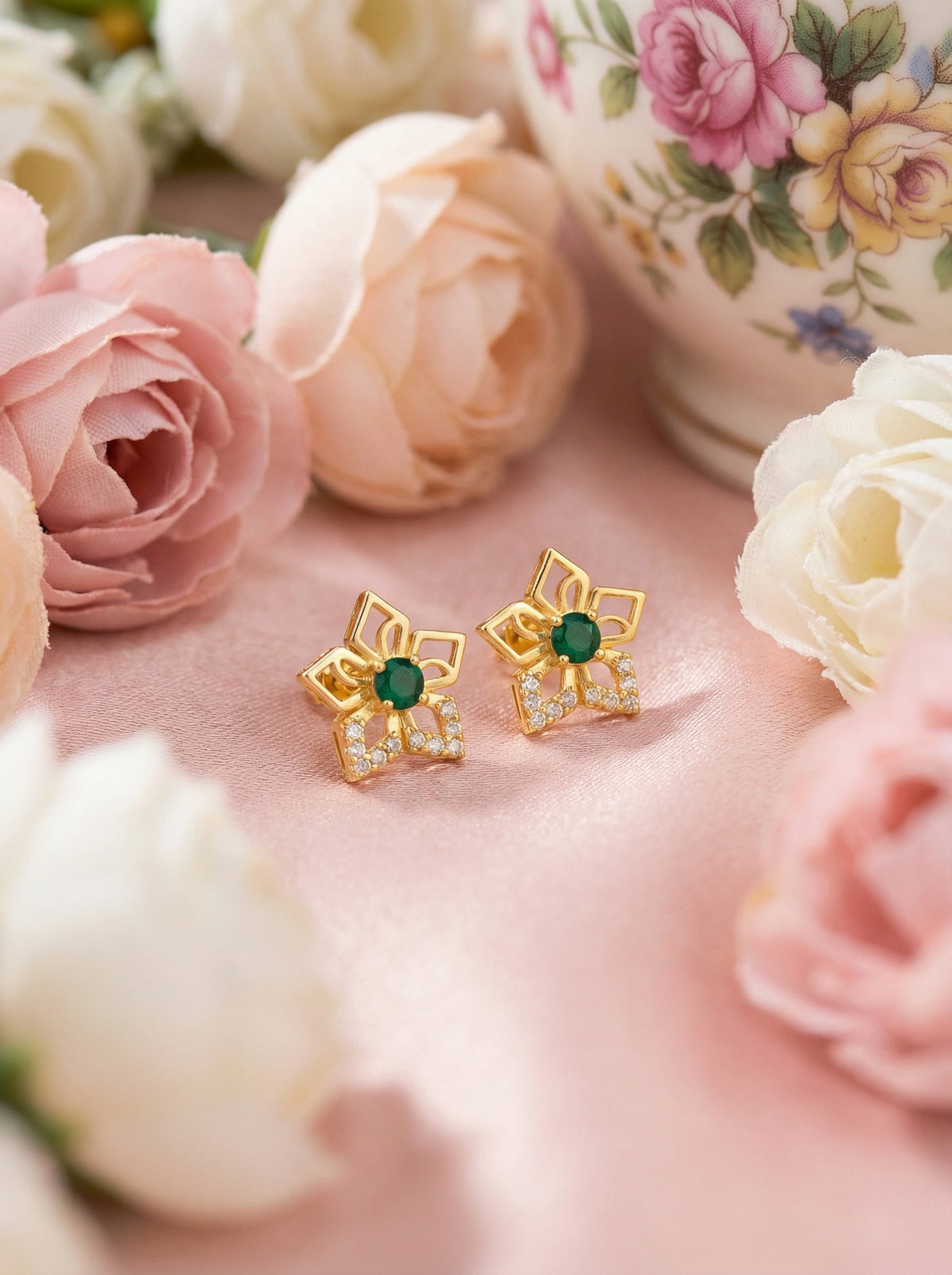 18k gold plated earrings with green gemstones on a pink surface with flowers