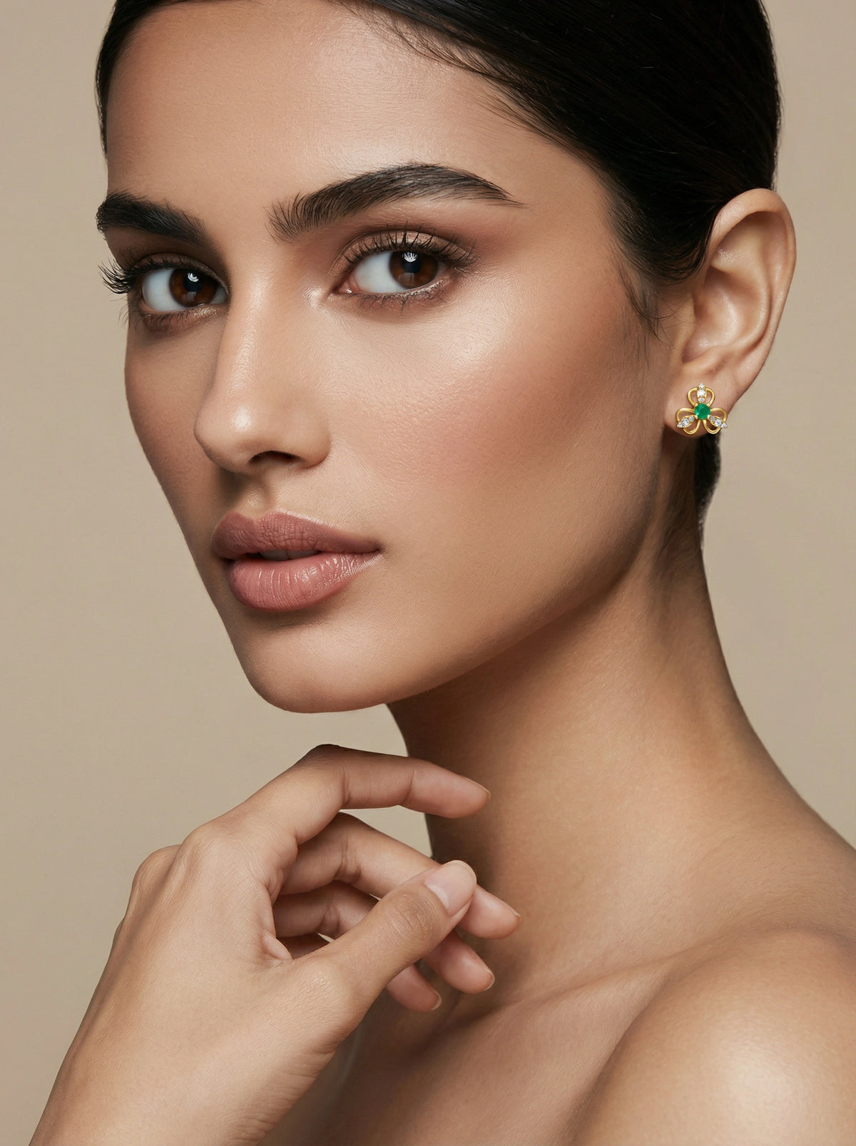 close-up of a woman wearing a 18k gold plated  green gemstone earring against a beige background