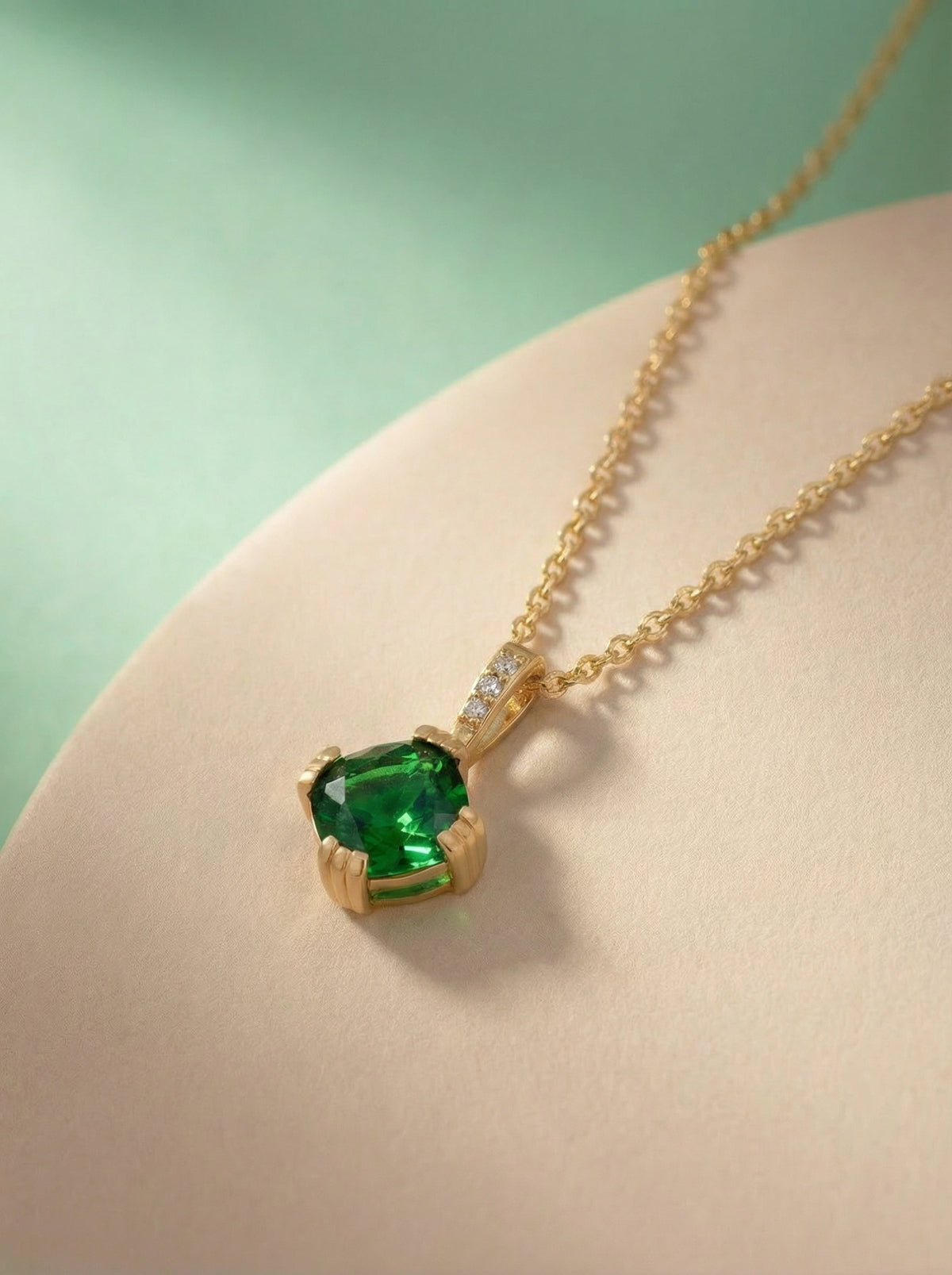18k gold plated necklace with a green gemstone pendant on a light pink surface.