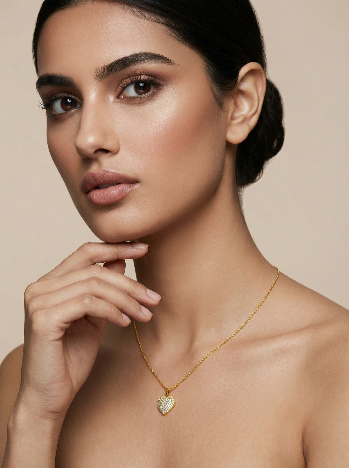 woman wearing a 18k  gold plated necklace with a heart pendant against a beige background