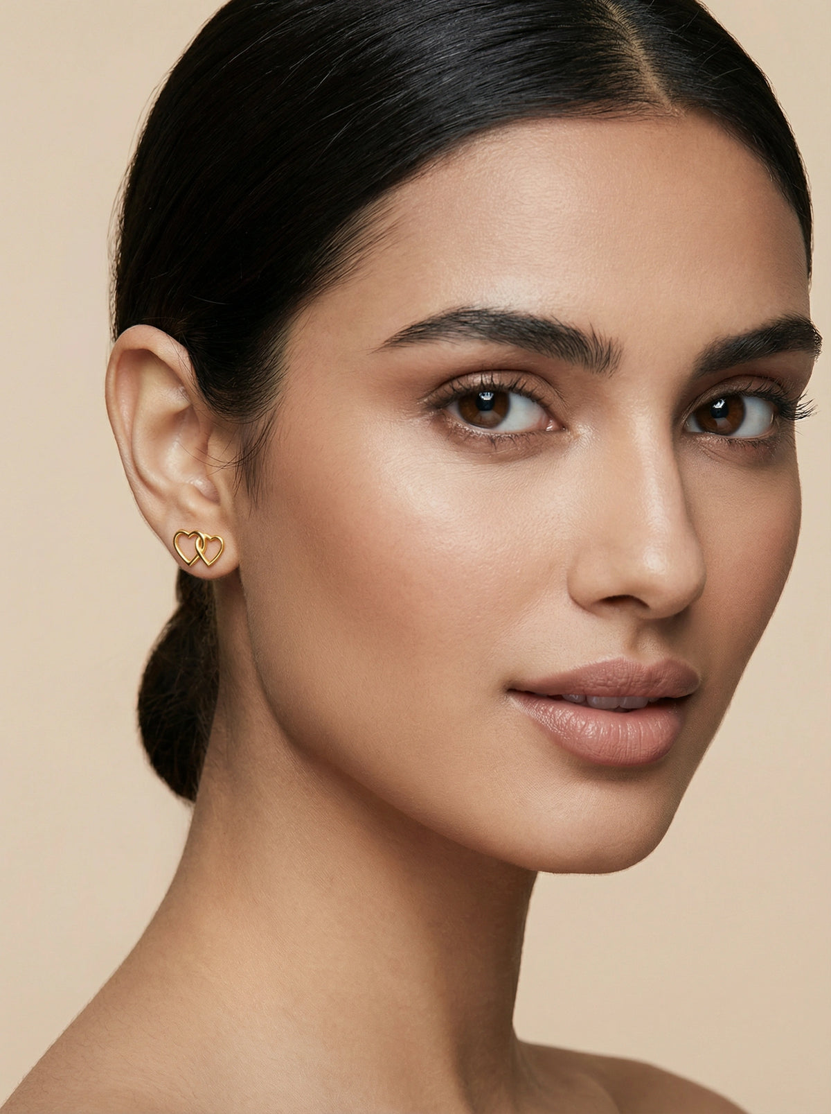 woman wearing a 18k gold plated heart-shaped earring against a beige background