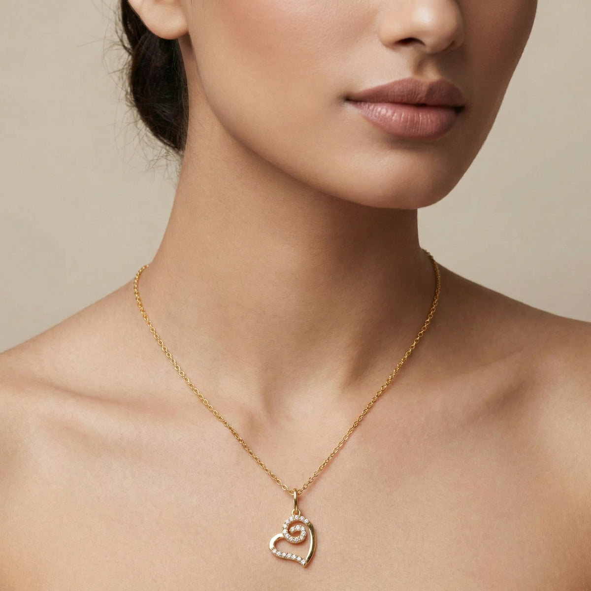 close-up of a woman wearing a 18k gold plated necklace with a heart-shaped pendant against a neutral background