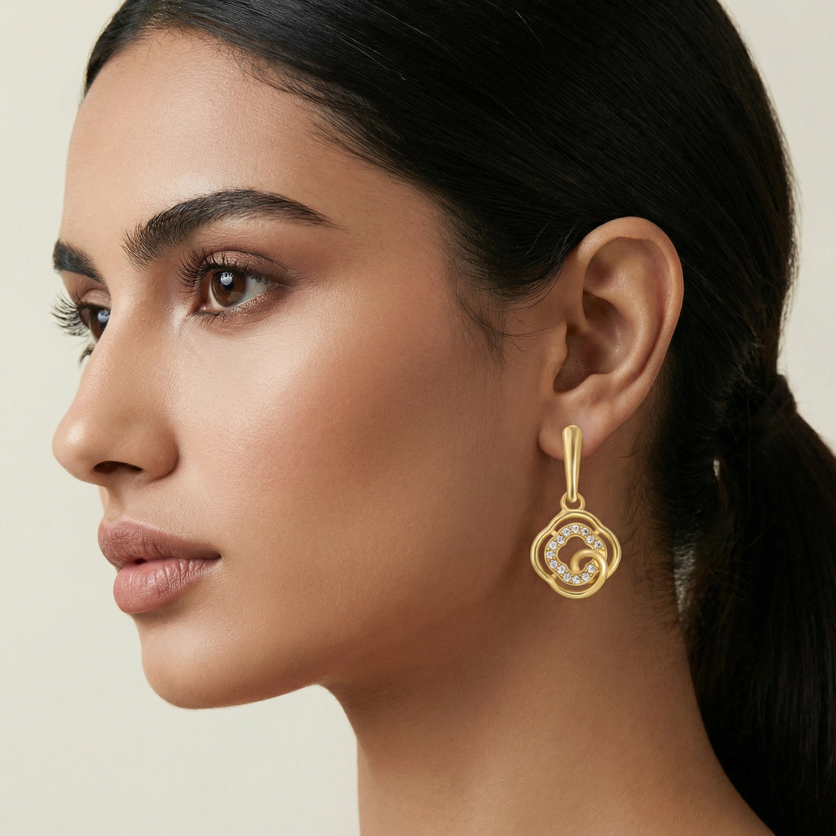 close-up of a woman wearing a 18k gold plated earring with a beige background