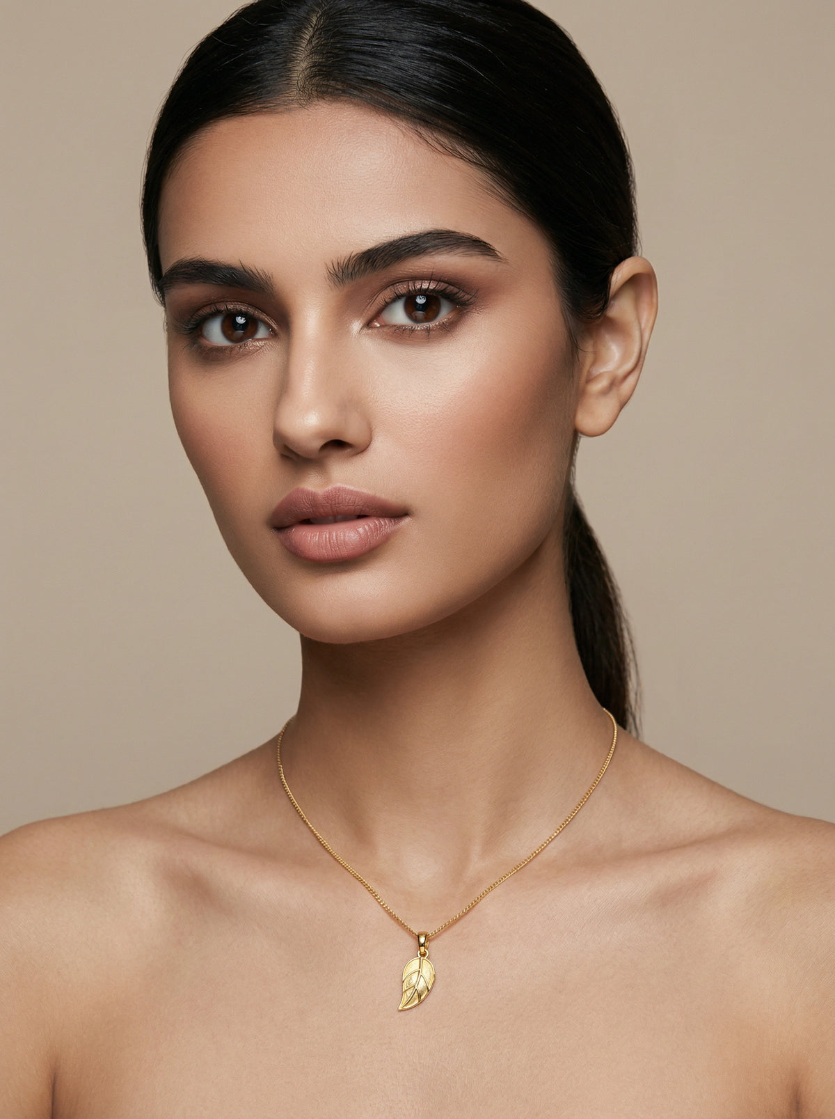 woman wearing a 18k gold plated necklace with a leaf pendant against a neutral background