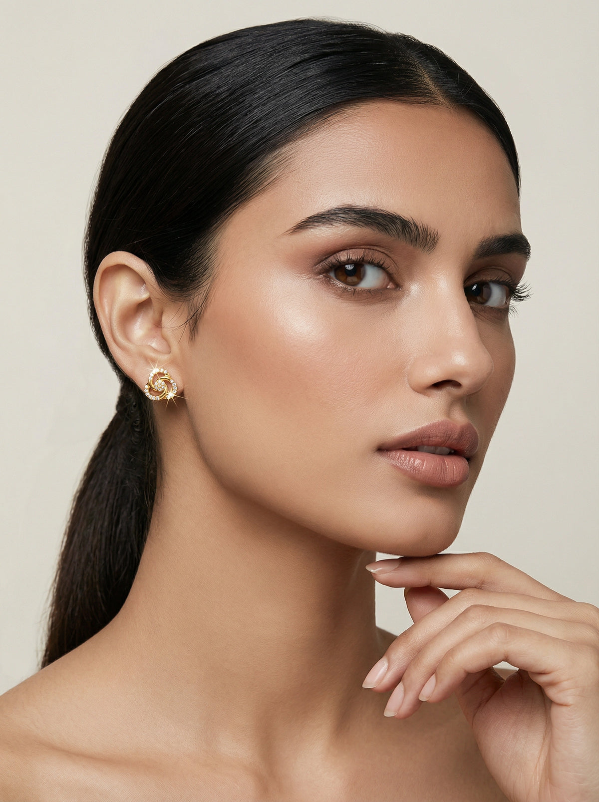 woman with a ponytail wearing 18k  gold plated earrings against a neutral background