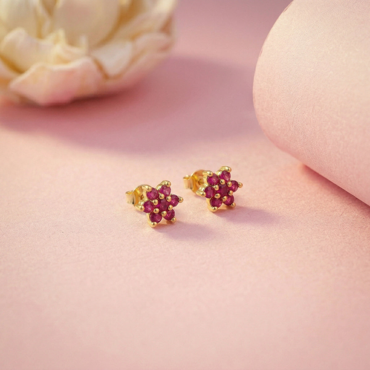 18k gold plated  earrings with red gemstones on a pink surface