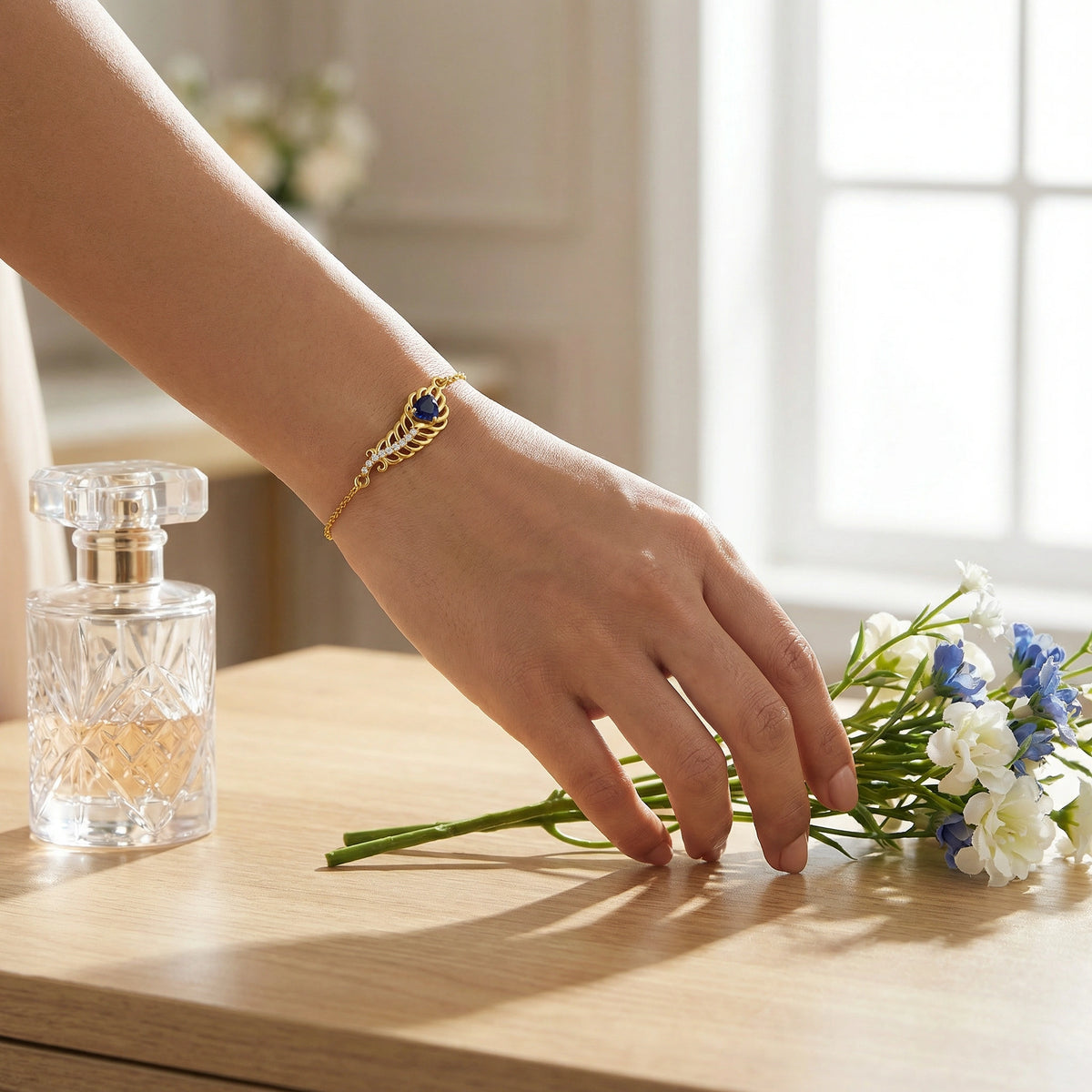 hand wearing a  18k gold plated bracelet with a blue stone, holding flowers on a wooden surface with a perfume bottle.