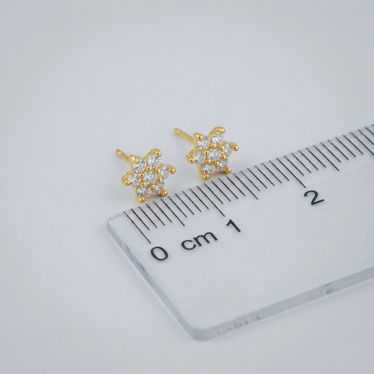 18k Gold plated arrings with clear stones on a ruler for scale, on a light gray background