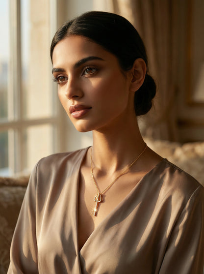 Woman wearing a beige top and 18k gold plated necklace in a softly lit room.