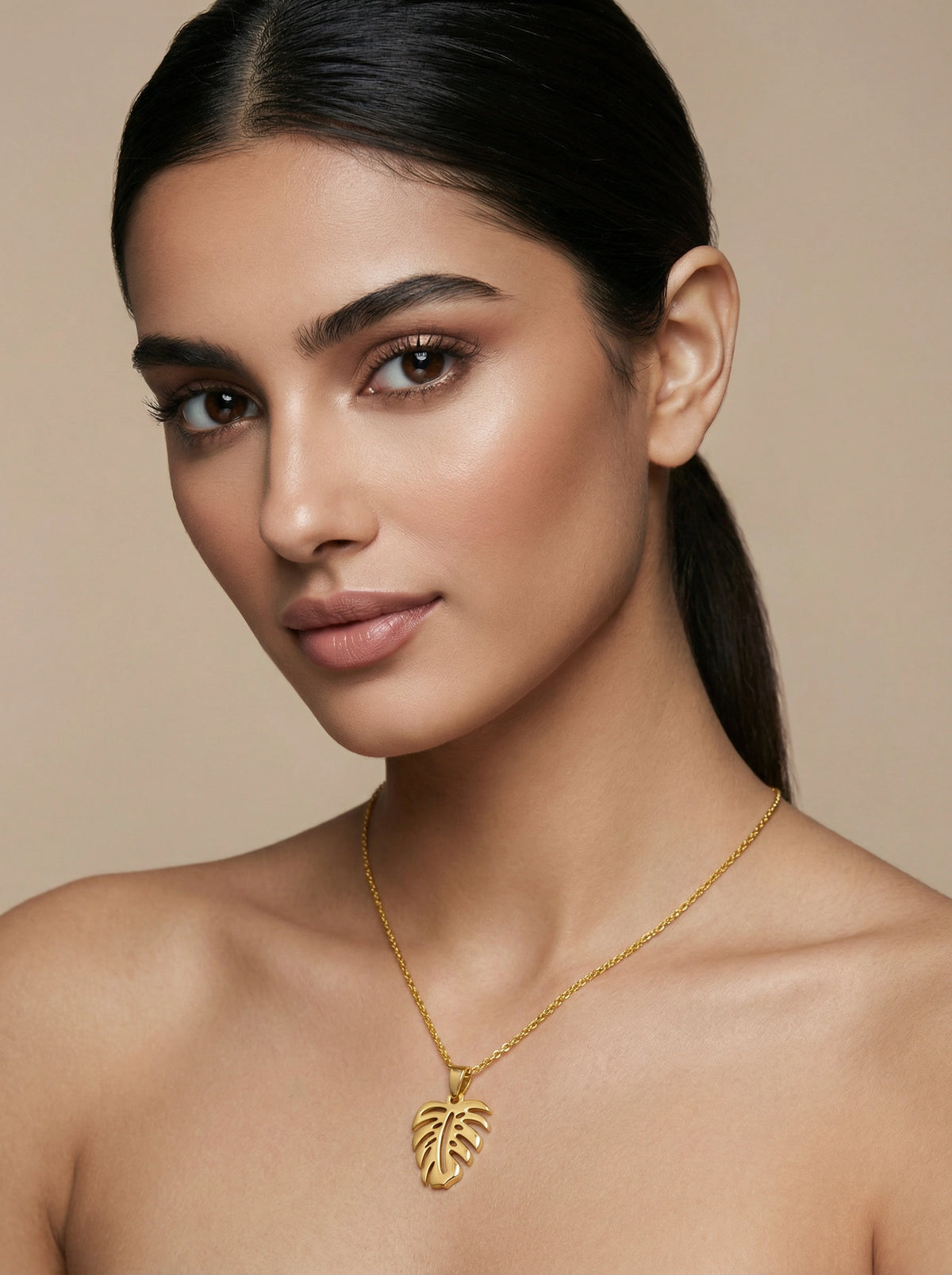 woman wearing a 18k gold plated  necklace with a leaf pendant against a beige background