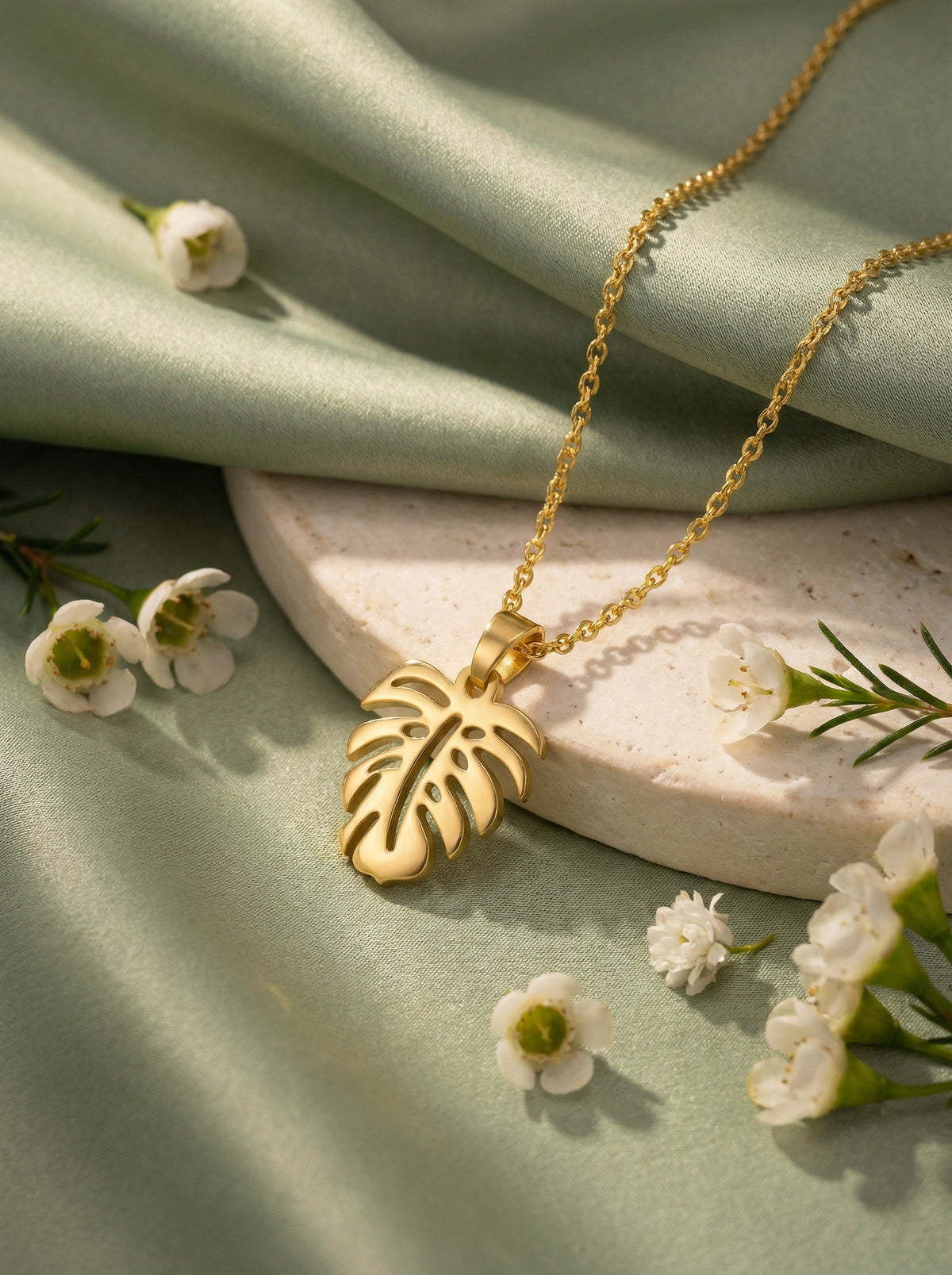 18k gold plated leaf necklace on a light green fabric background with small white flowers