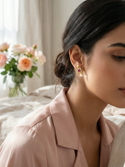 Woman wearing 18k gold plated earrings with a blurred background of flowers and light curtains