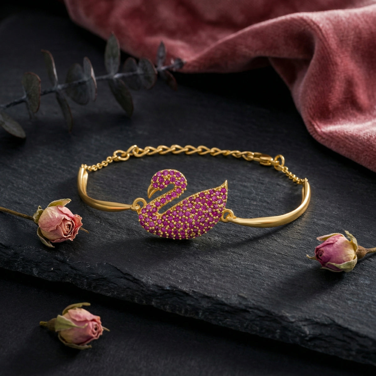 18k gold plated  bracelet with a pink swan design on a dark surface with flowers and a red fabric background.