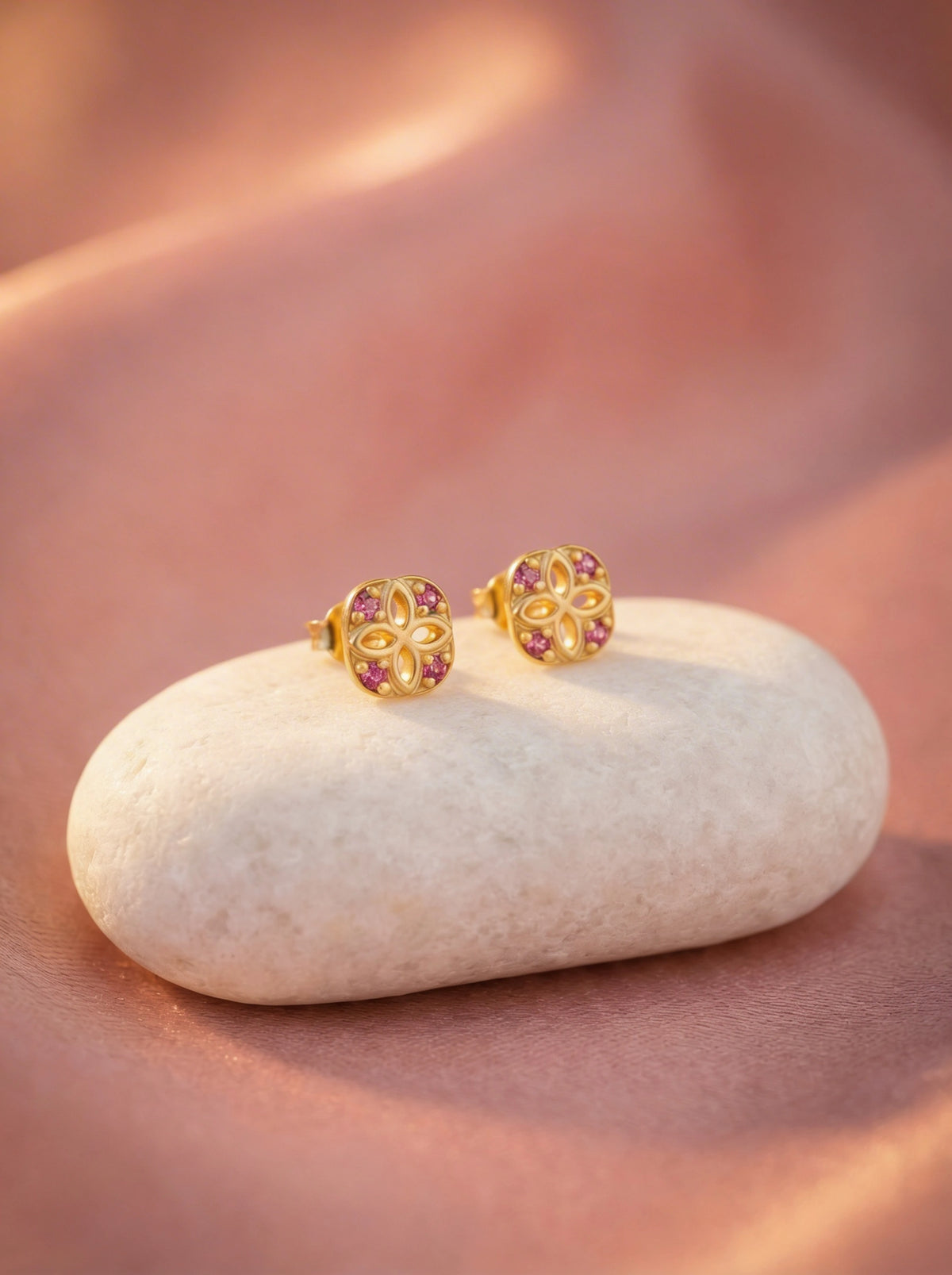 18k gold plated  earrings with pink gemstones on a white stone against a soft pink background