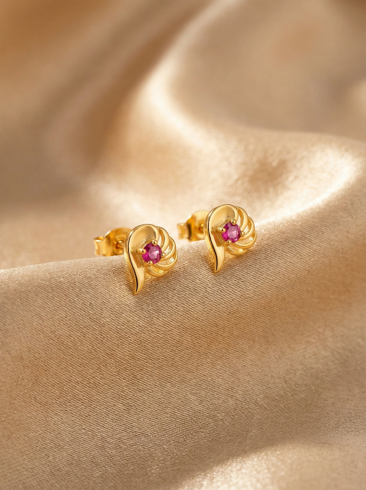 18k gold plated earrings with pink gemstones on a beige fabric background