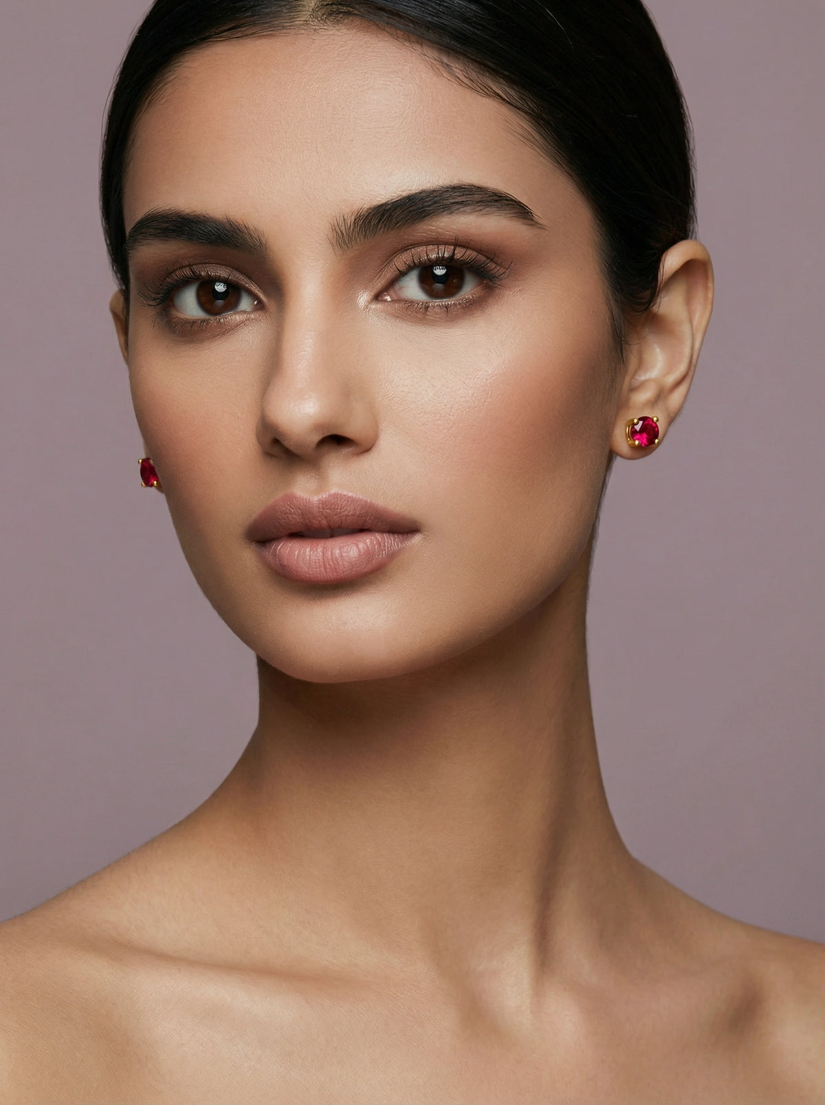 close-up of a woman wearing 18k gold plated red earrings against a neutral background