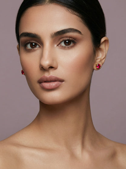 Close-up of a woman wearing 18k gold plated red earrings against a neutral background