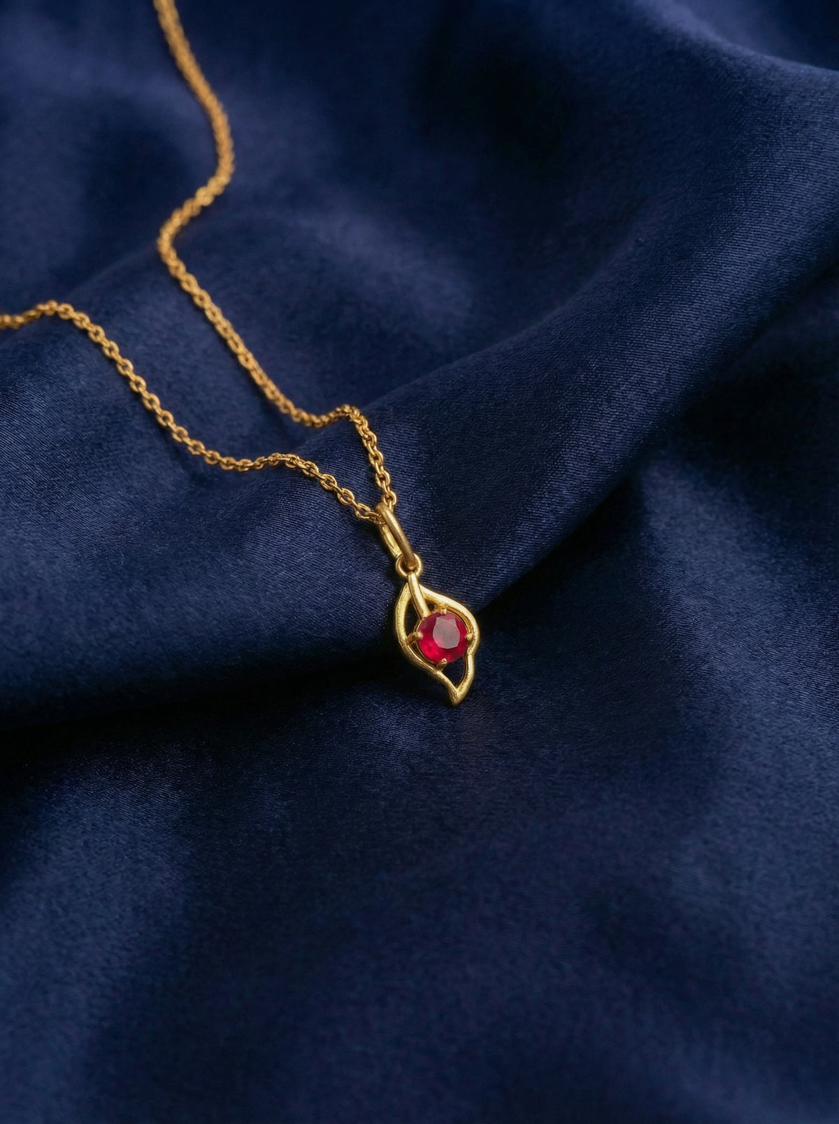 18k gold plated necklace with a red gemstone pendant on a dark blue fabric background