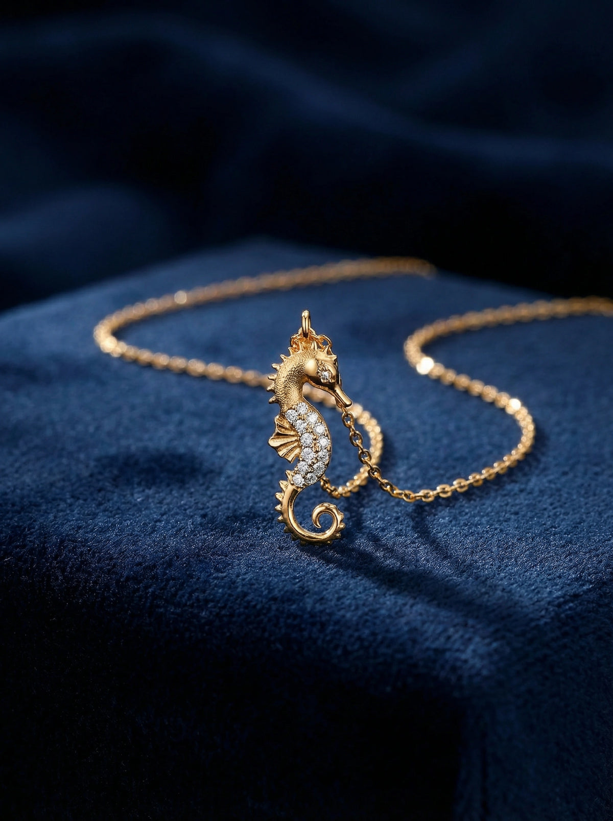 18k gold plated seahorse necklace with diamonds on a blue fabric background