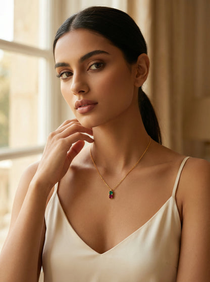 Woman wearing a 18k gold plated necklace with a colorful pendant in a softly lit room.