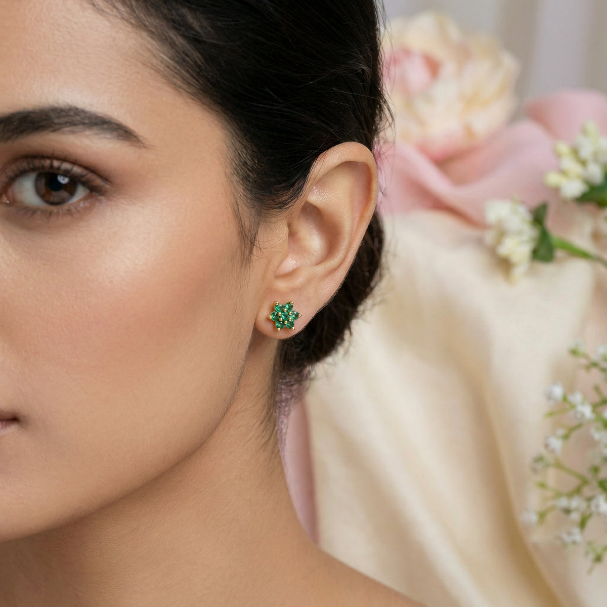 Close-up of a woman wearing green 18k gold plated earrings with a blurred floral background