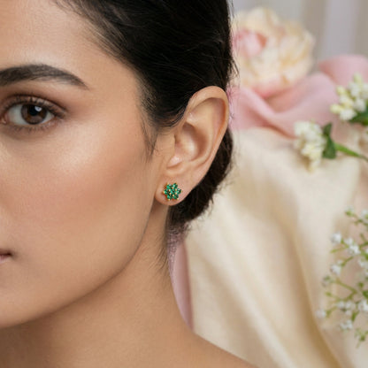Close-up of a woman wearing green 18k gold plated earrings with a blurred floral background