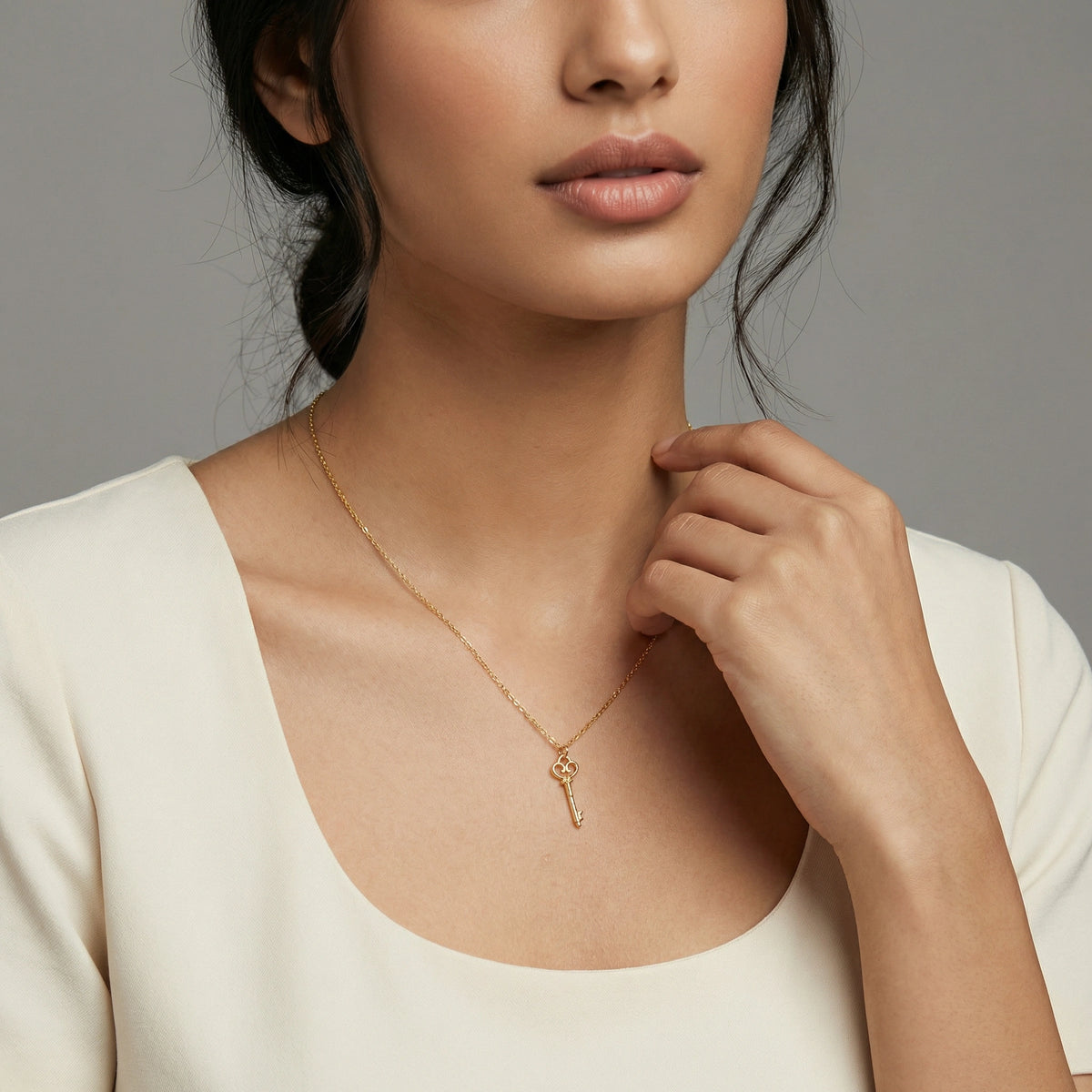 woman wearing a 18k gold plated necklace with a key pendant against a neutral background