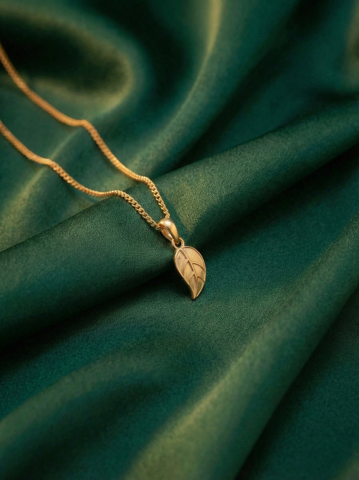 18k gold plated necklace with a leaf pendant on a green fabric background