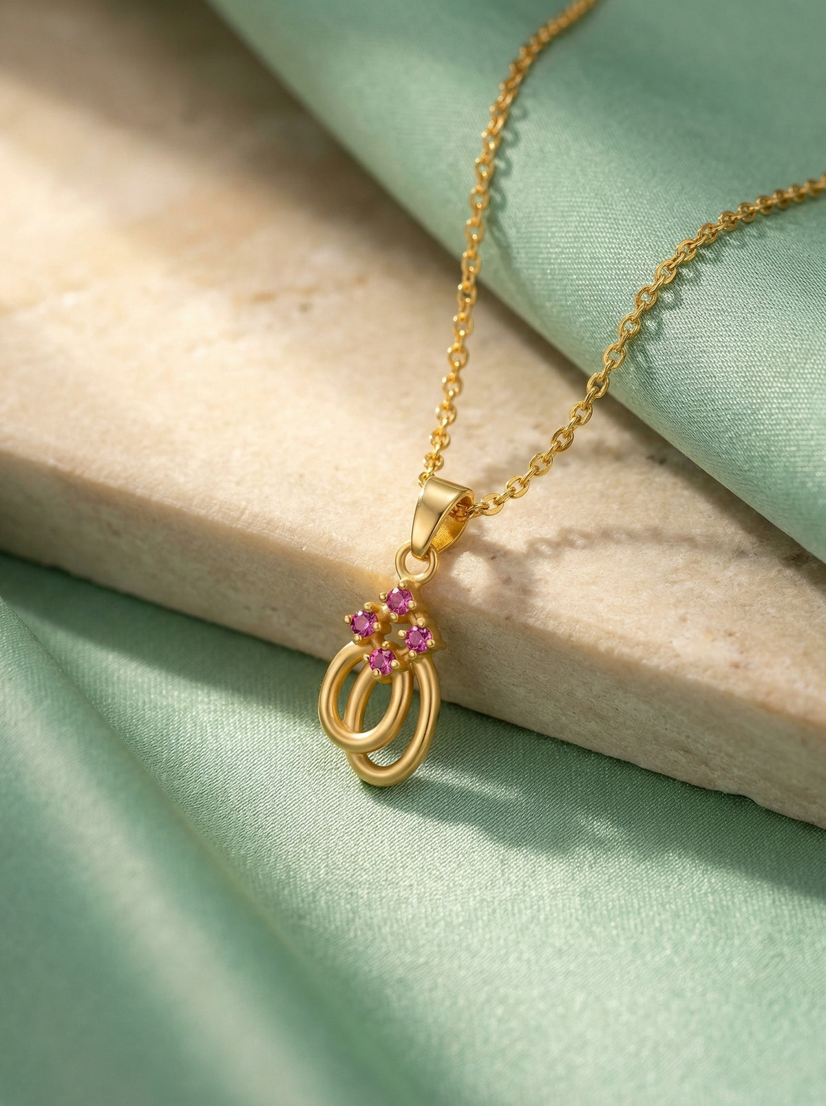 18k gold plated necklace with a pendant featuring pink gemstones on a light green fabric background