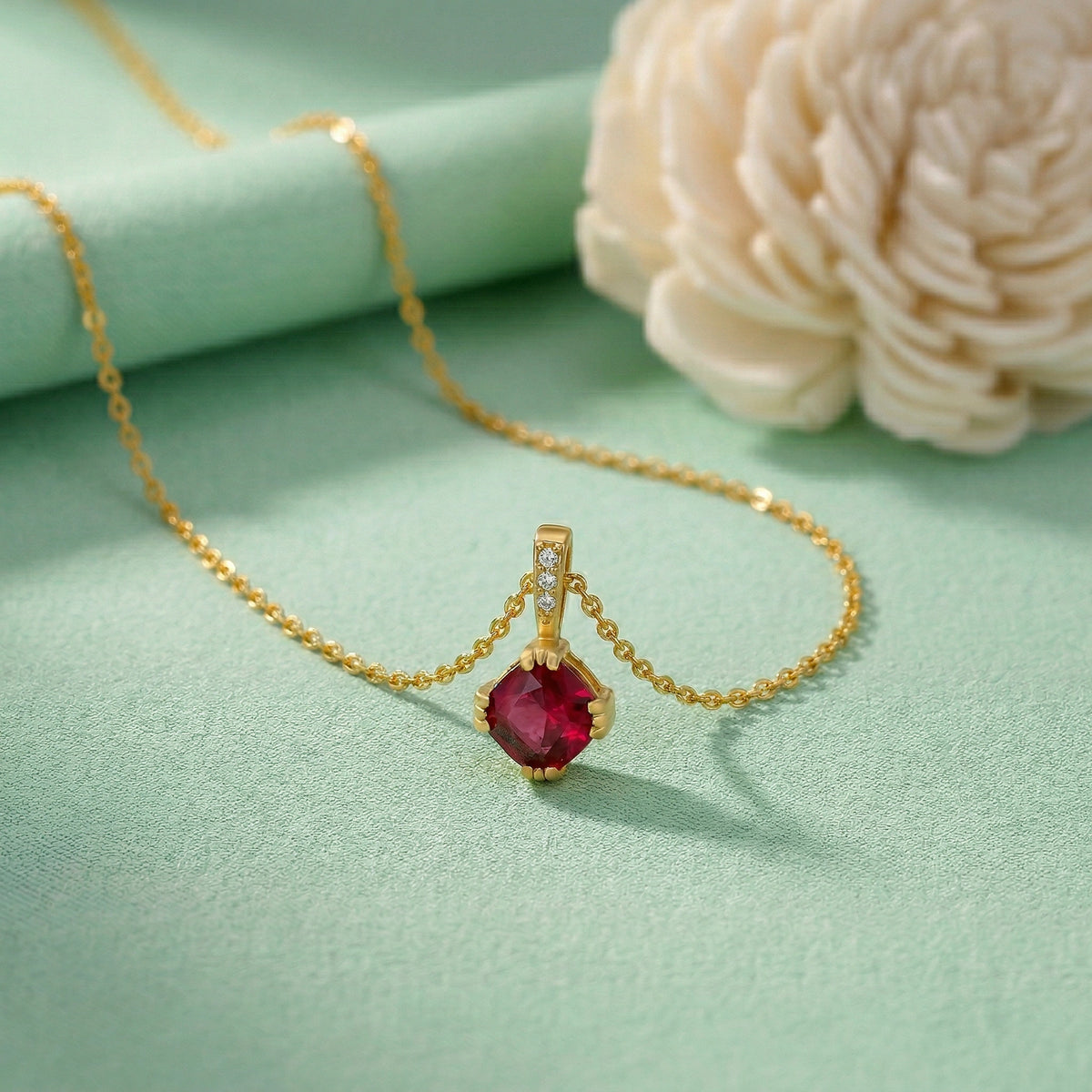 18k gold plated necklace with a red gemstone pendant on a light green background