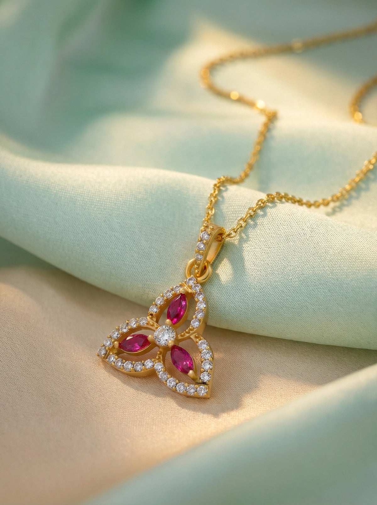 18k gold plated necklace with a heart-shaped pendant featuring red gemstones on a soft fabric background