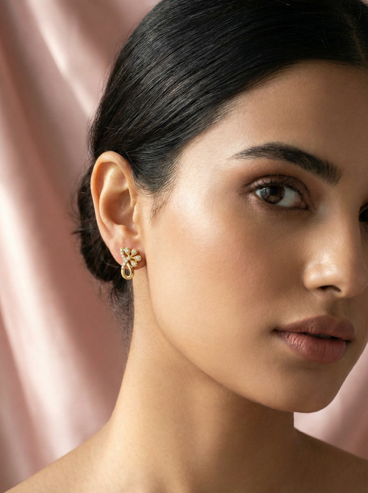 close-up of a woman wearing a 18k gold plated earring with a soft pink background