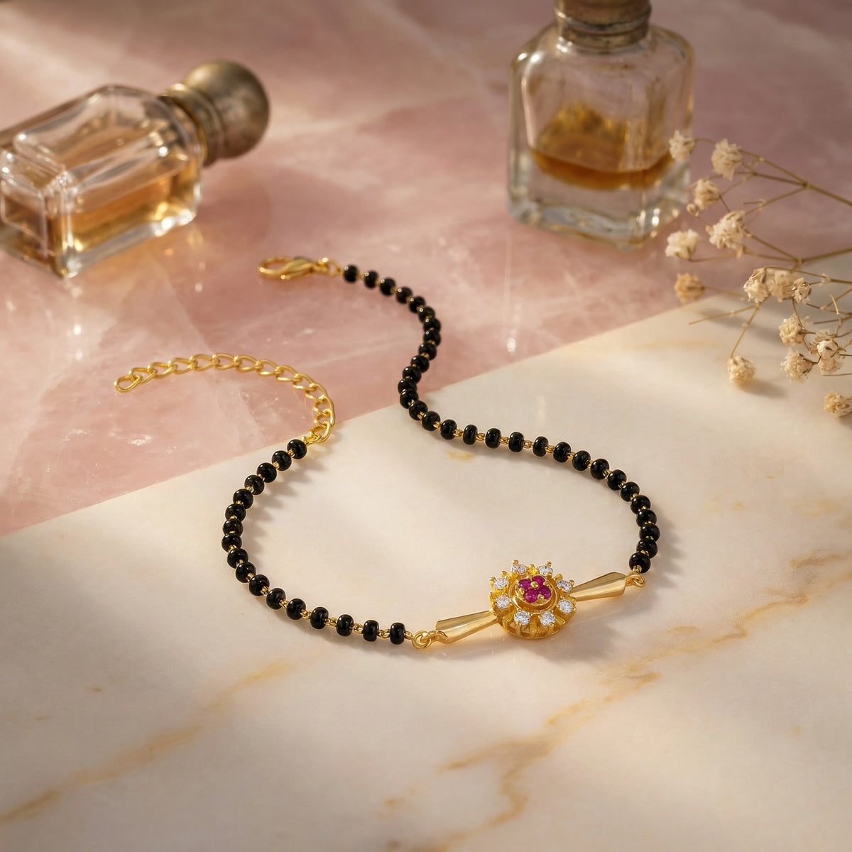black beaded bracelet with 18k gold plated accents on a marble surface with perfume bottles and flowers.
