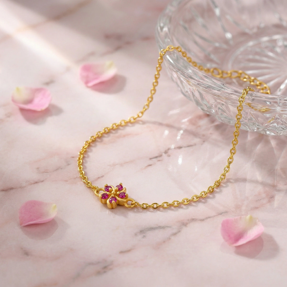 18k gold plated bracelet with a floral clasp on a marble surface with pink petals