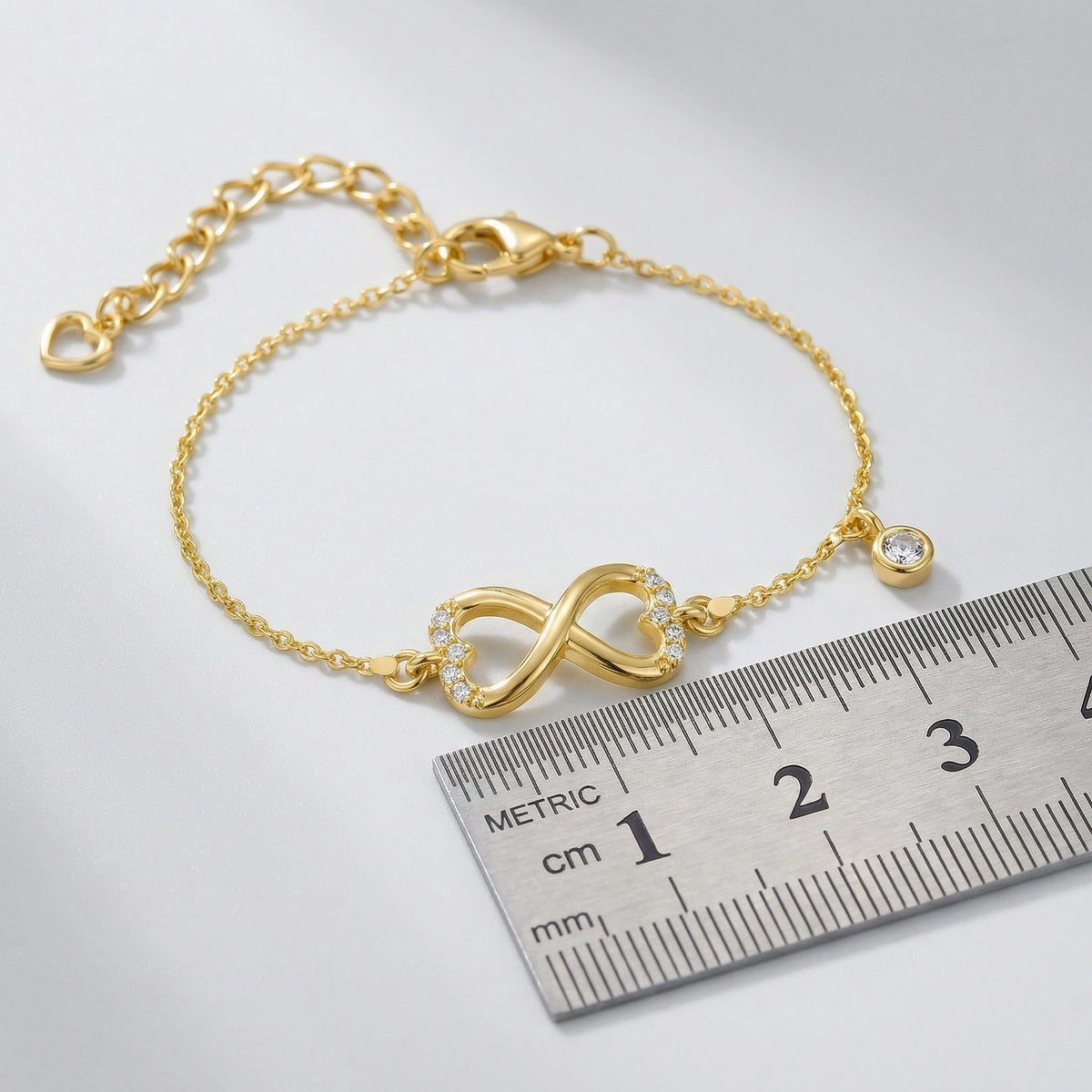18k gold plated bracelet with an infinity symbol next to a ruler on a white background