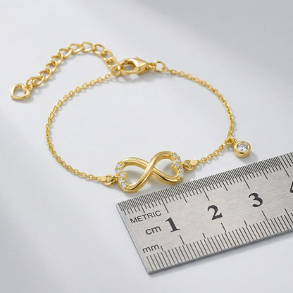 18k Gold plated bracelet with an infinity symbol next to a ruler on a white background