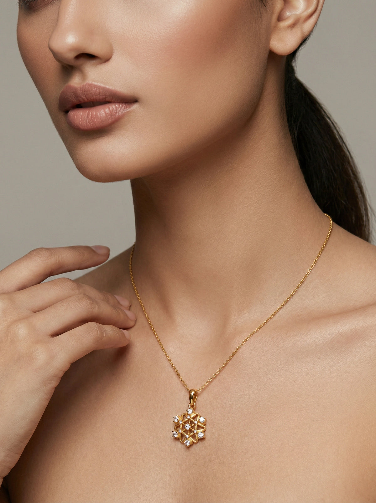 close-up of a person wearing a 18k gold plated necklace with a snowflake pendant against a neutral background