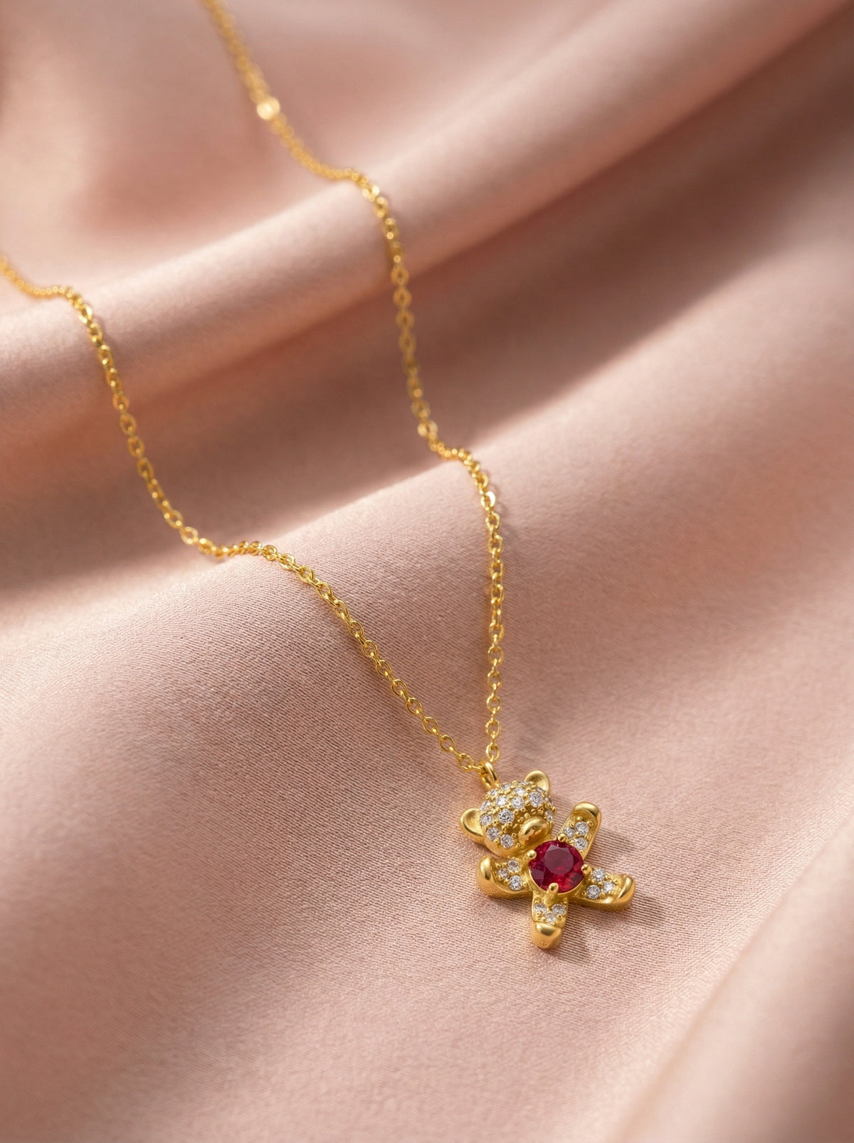 18k gold plated necklace with a red gemstone pendant on a pink fabric background