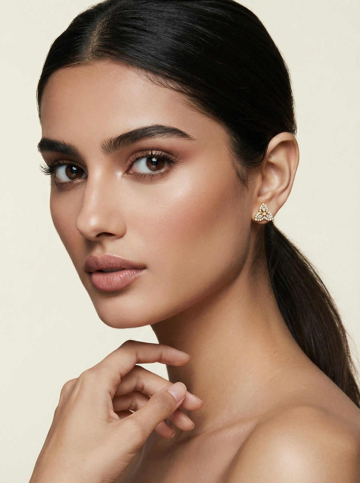 woman with a smooth neck and ear, wearing 18k gold plated earrings against a beige background