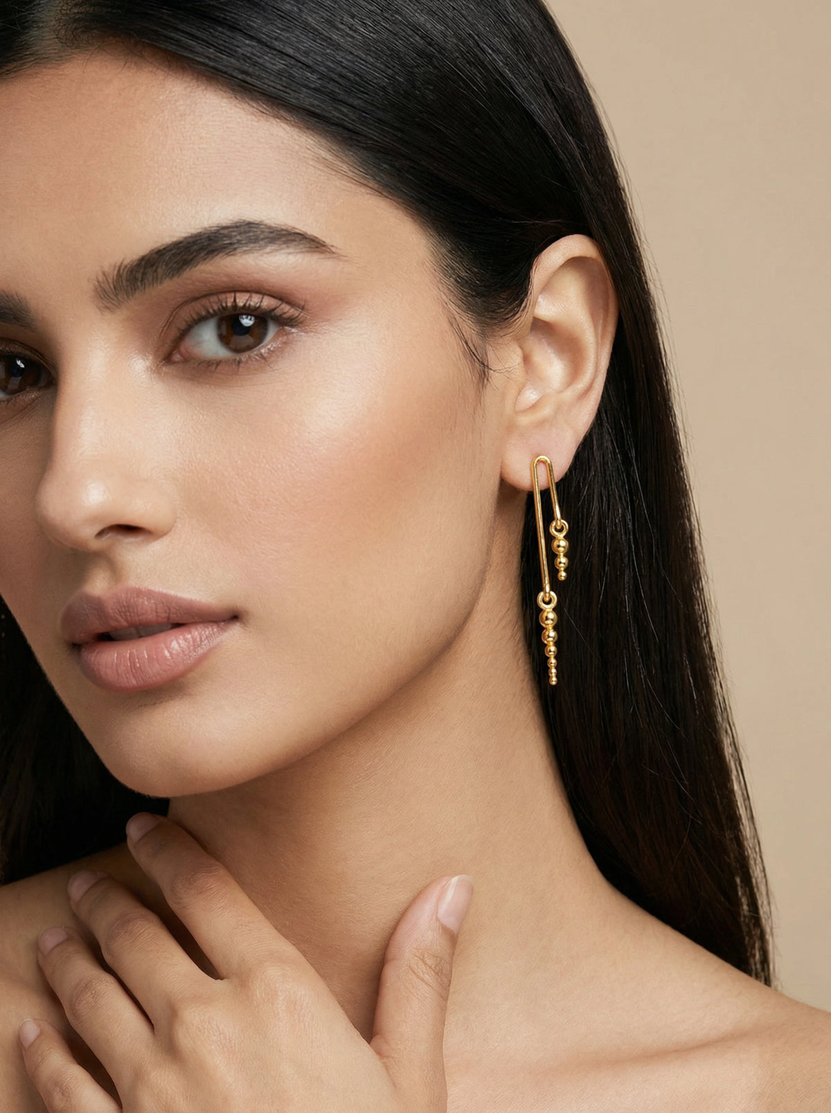 close-up of a woman wearing 18k gold plated earrings with a neutral background