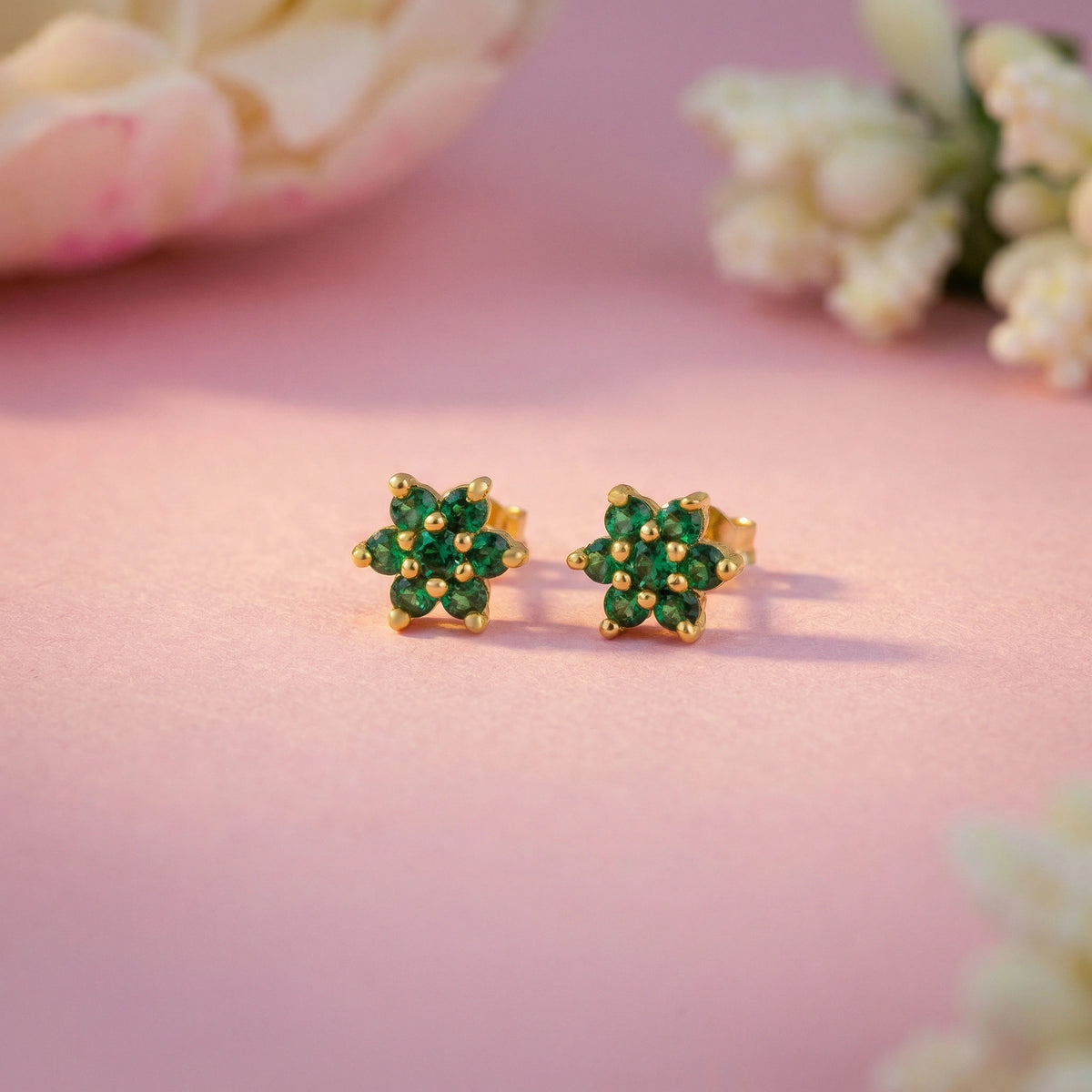 18k gold plated earrings with green gemstones on a pink background