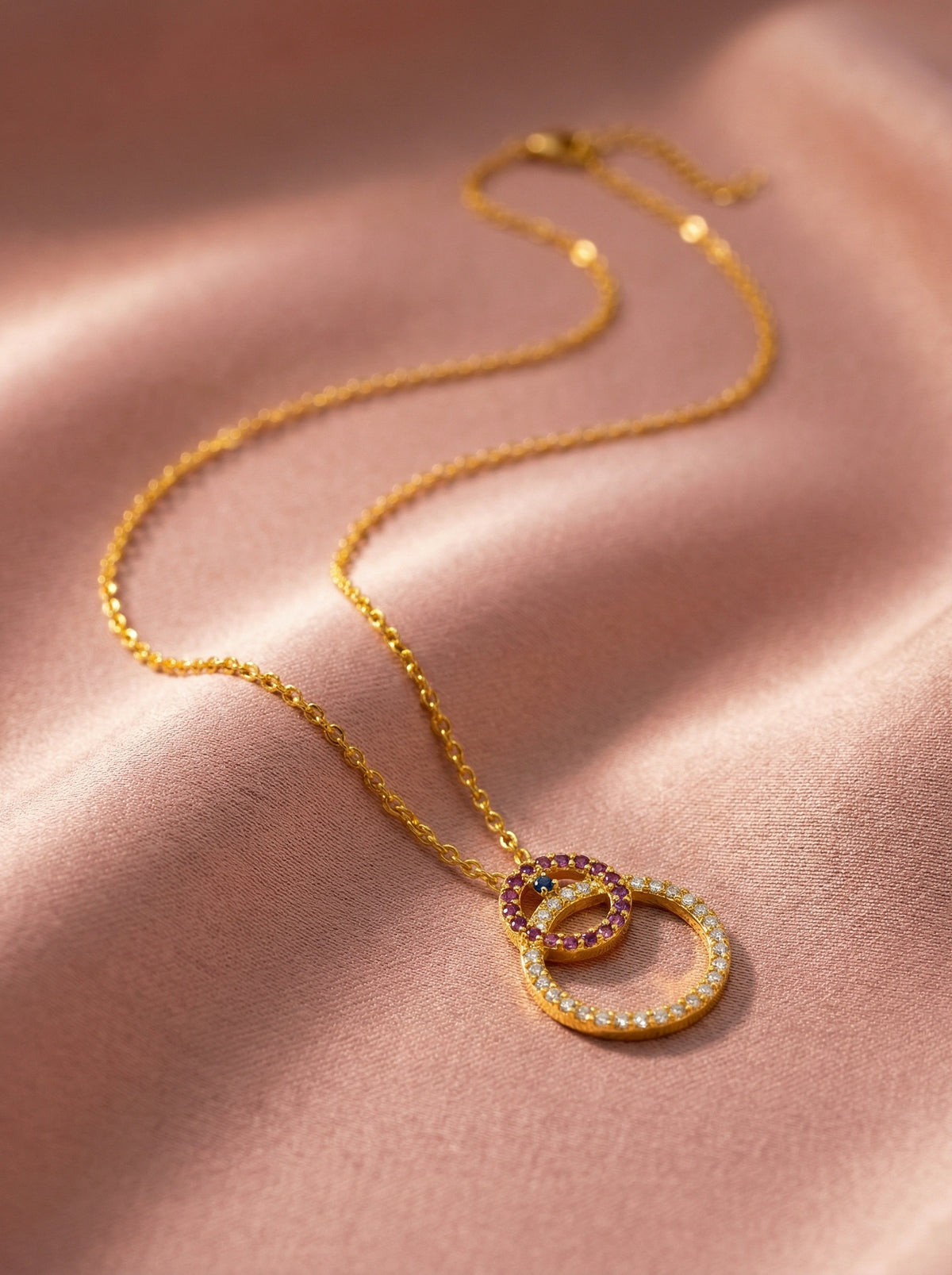 18k gold plated necklace with interlocking rings on a pink fabric background