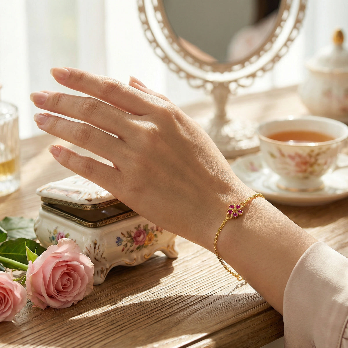 hand wearing 18k  gold plated  bracelet with pink flowers on a table with a teacup and roses.
