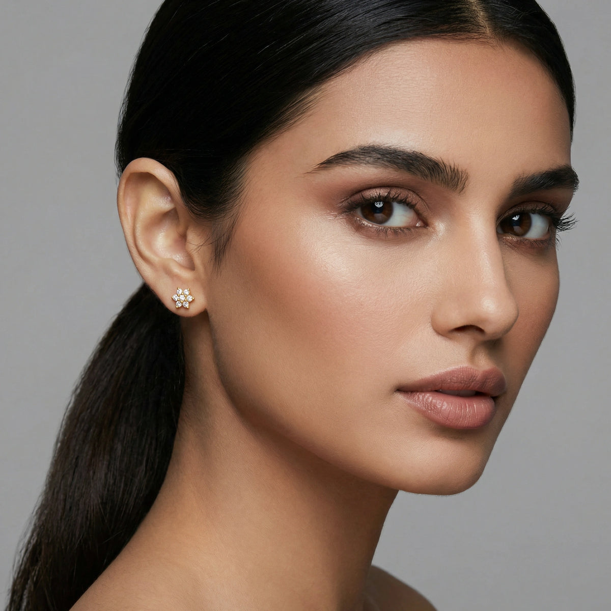 close-up of a woman wearing a 18k golde plated  earring against a gray background
