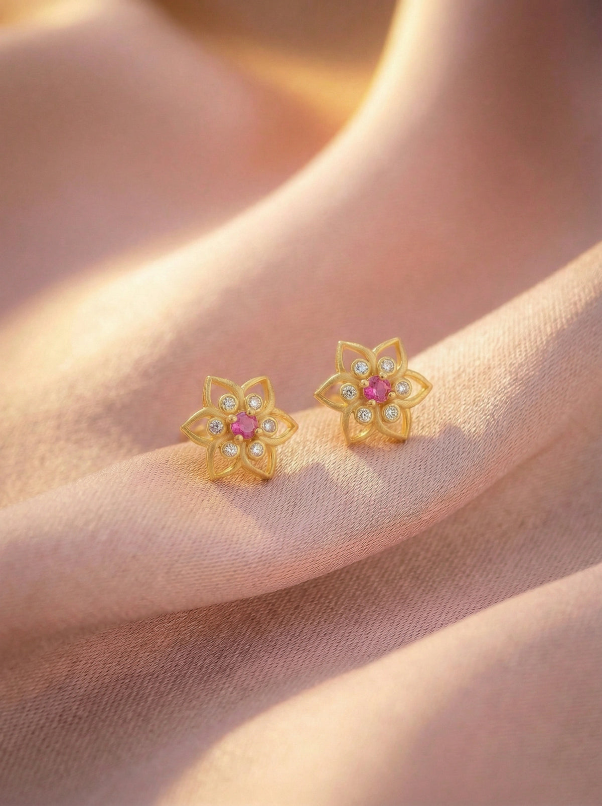 18k gold plated flower-shaped earrings with pink centers on a soft pink background