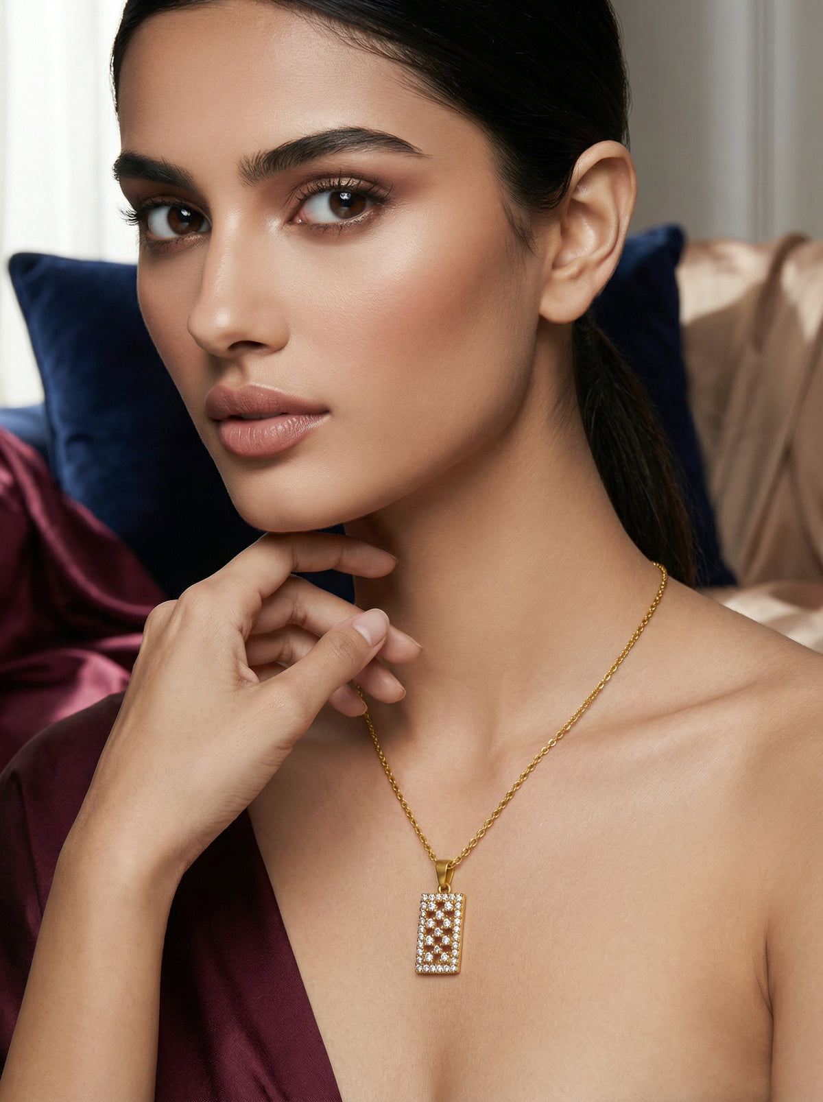 woman wearing a 18k gold plated necklace with a rectangular pendant, sitting on a couch.